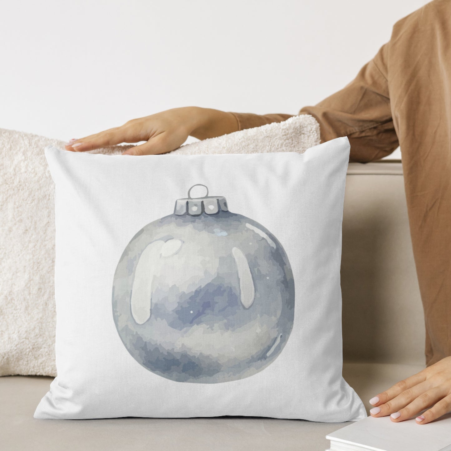 White pillow with a blue ornament design held by a person on a couch.
