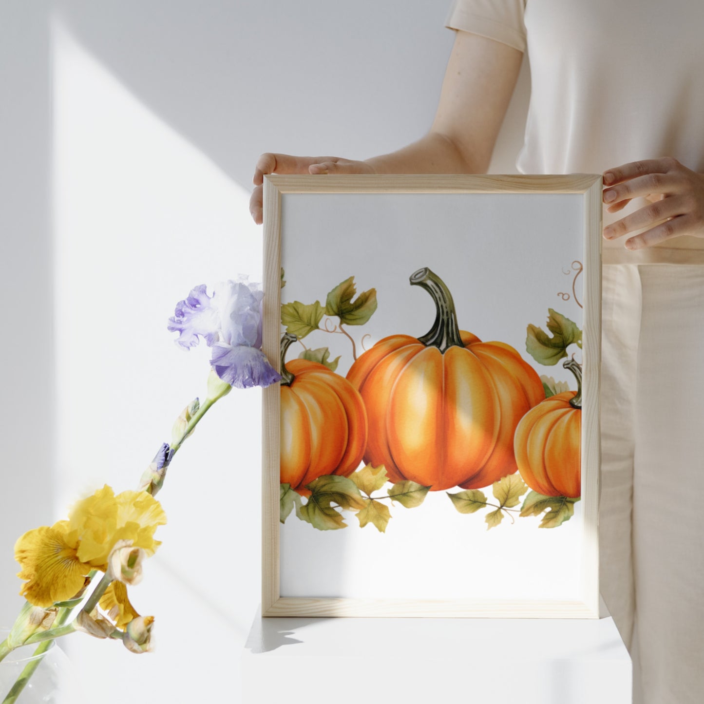 Person holding a framed artwork of pumpkins and flowers on a white background