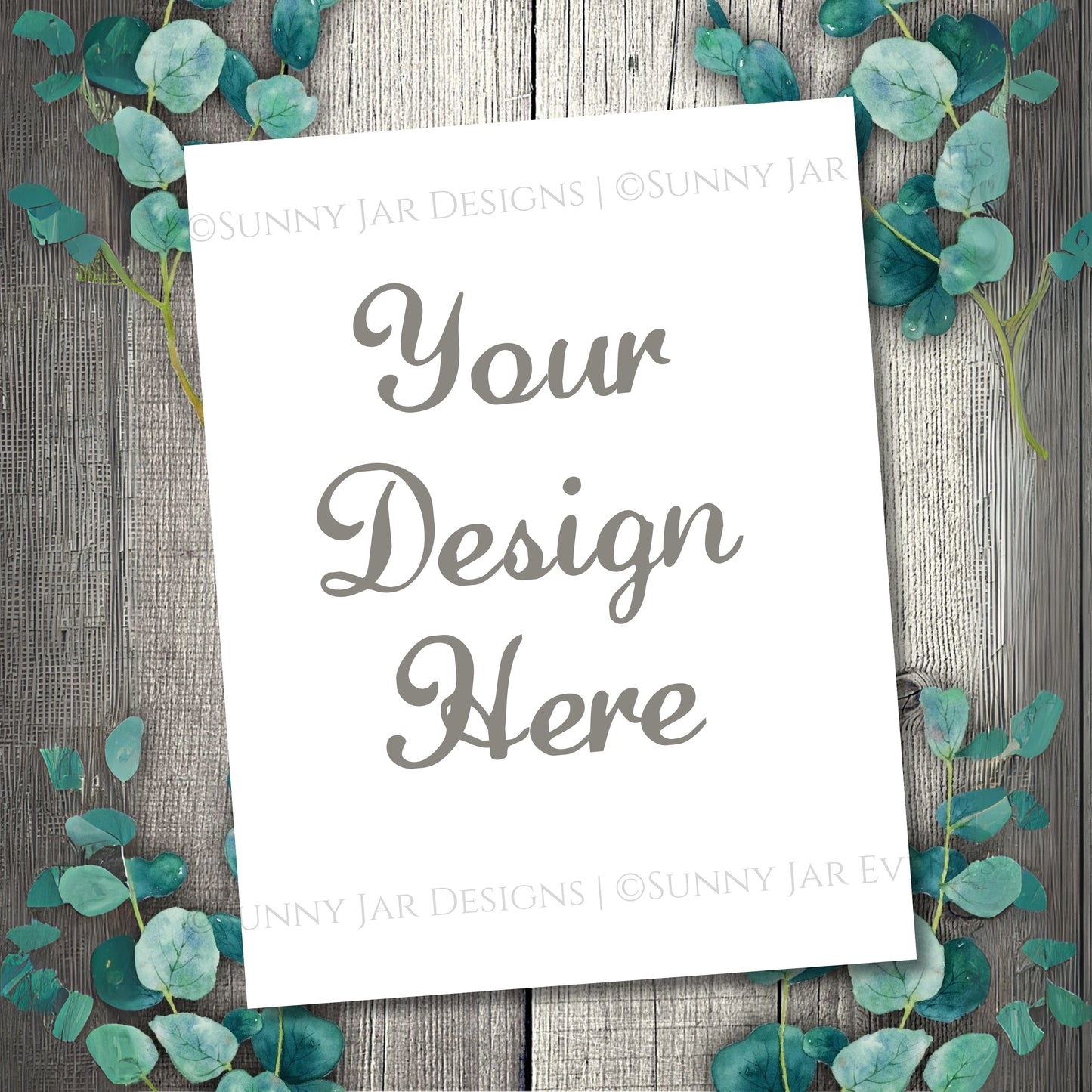 White paper with 'Your Design Here' text on a wooden background with eucalyptus leaves.