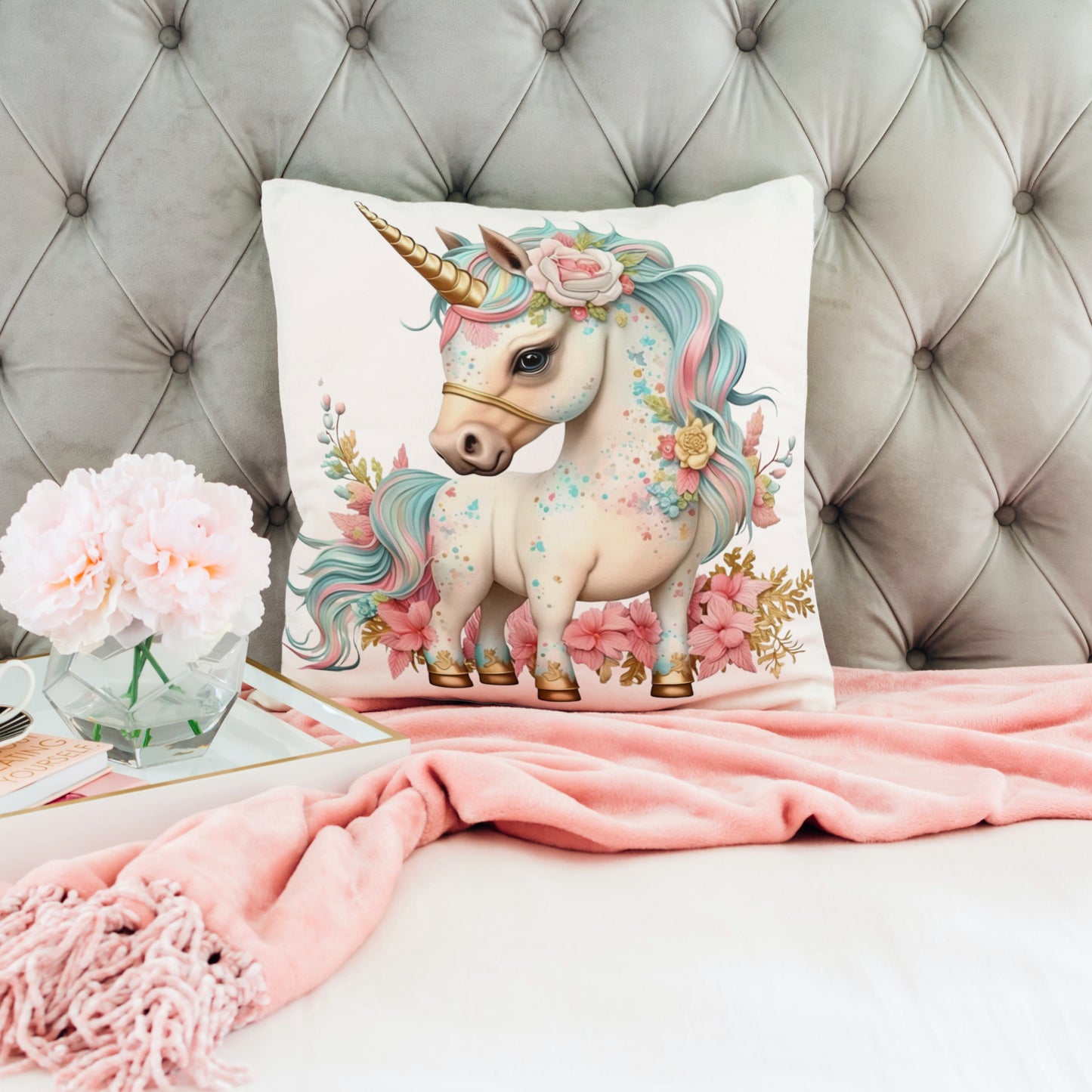 Decorative pillow with a unicorn design on a couch with pink blanket and flowers.