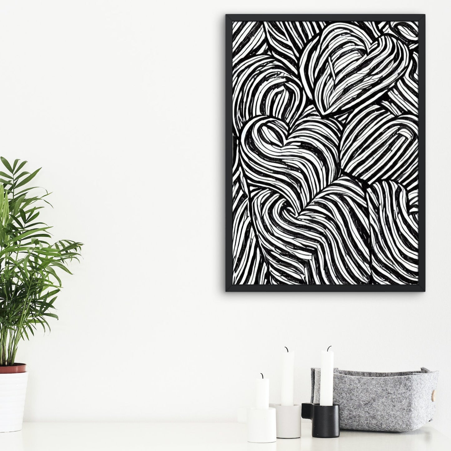 Framed black and white abstract art piece on a white wall with a plant and candles below.