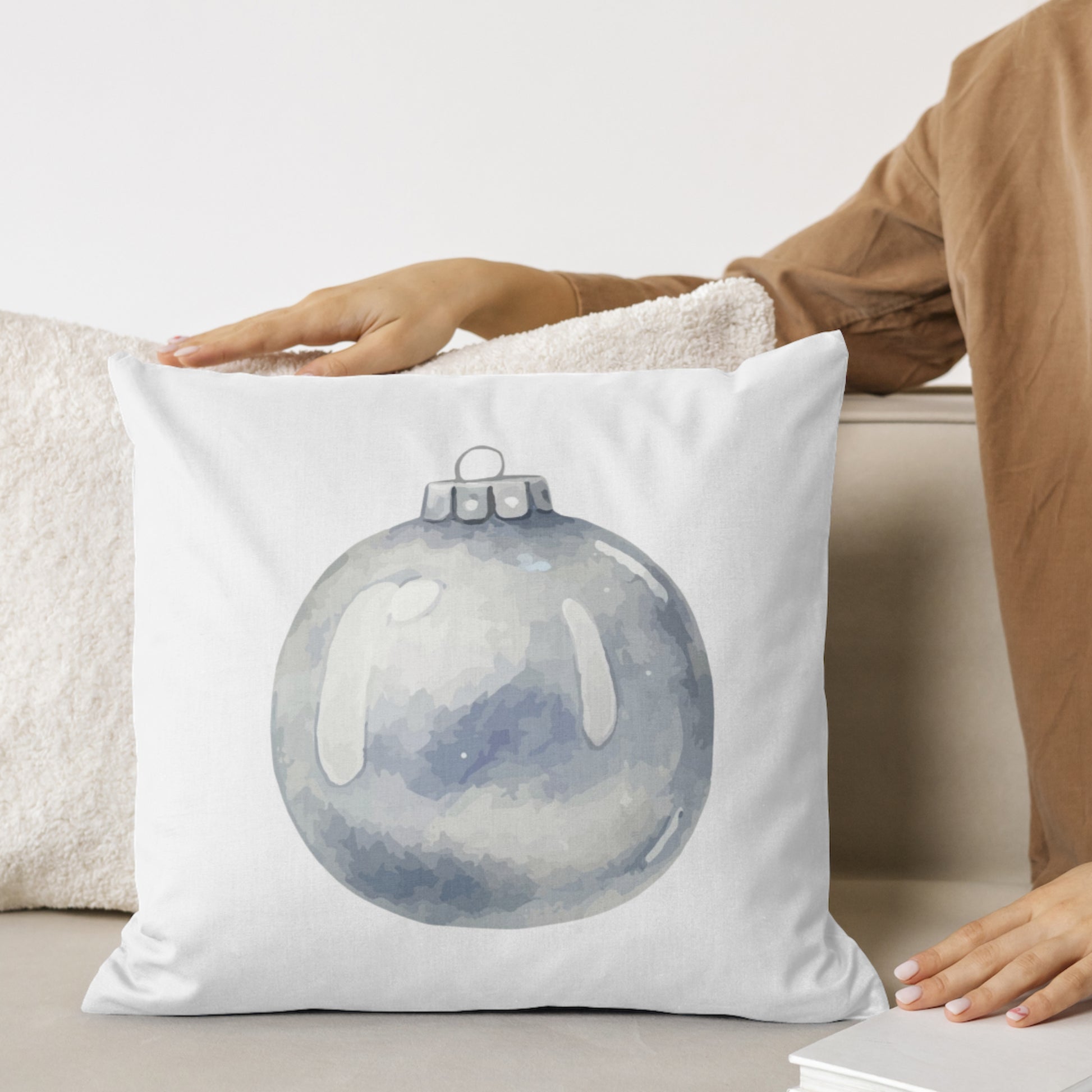White pillow with a blue ornament design held by a person on a couch.