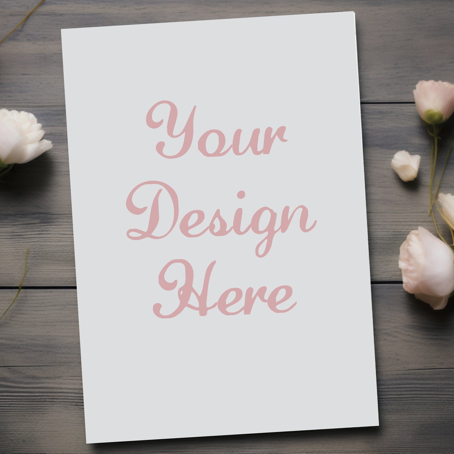 White paper with 'Your Design Here' text on a wooden surface with flowers.