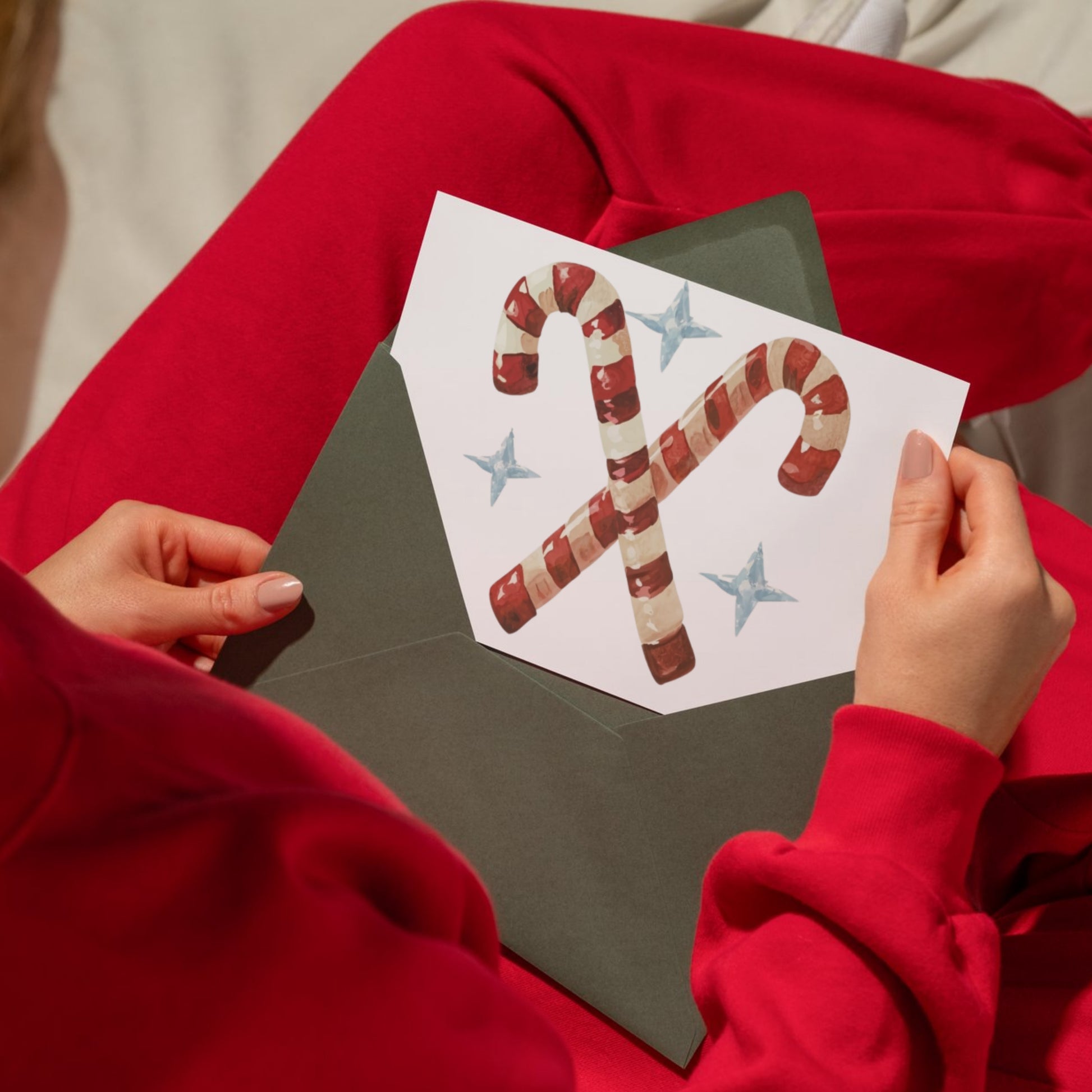 Person wearing a red sweater holding a card with candy canes and stars.