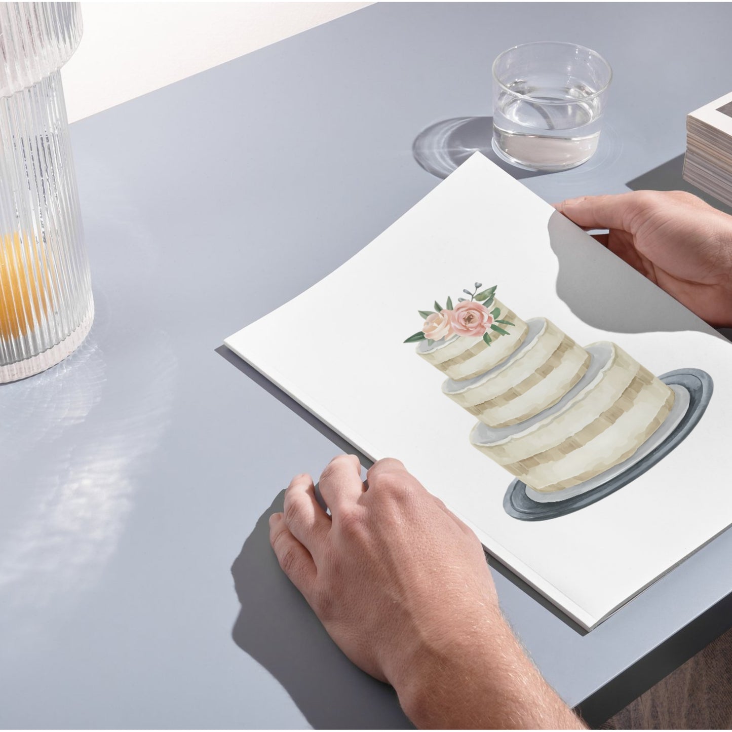 Person holding a card with a cake illustration on a table.