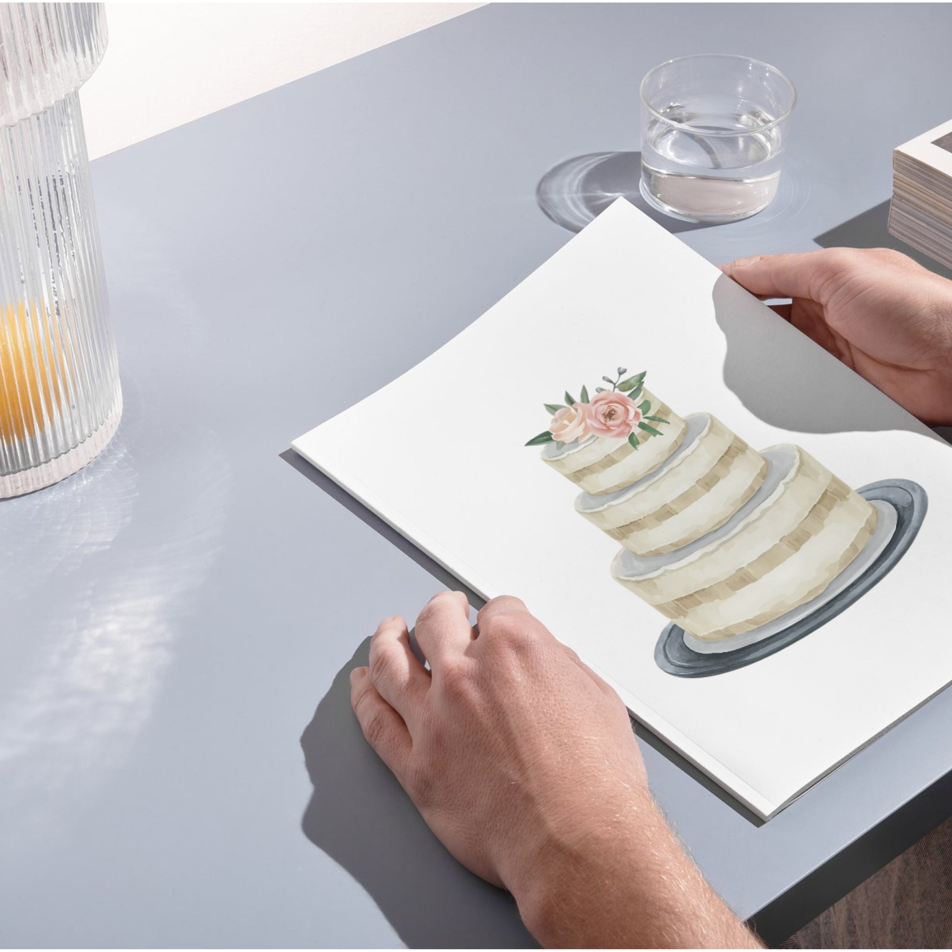 Person holding a card with a cake illustration on a table.